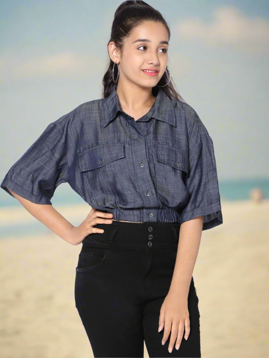 A young woman wearing a blue denim shirt with a collar and 3/4th sleeves, paired with black pants.